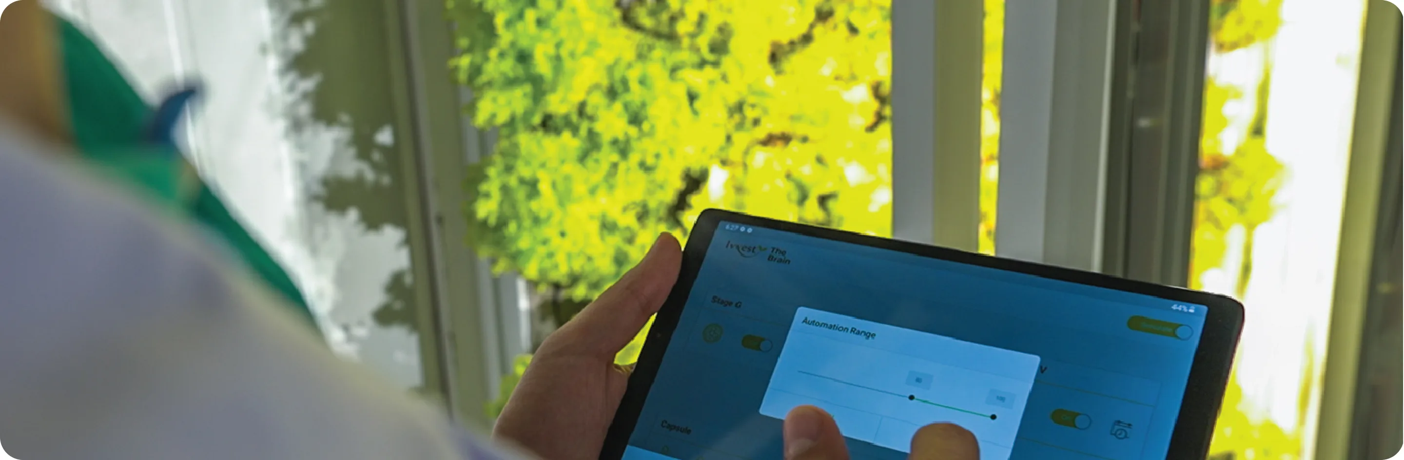 An operator holding a tablet running IvvestOS while standing inside The Capsule, with rows of leafy greens growing behind